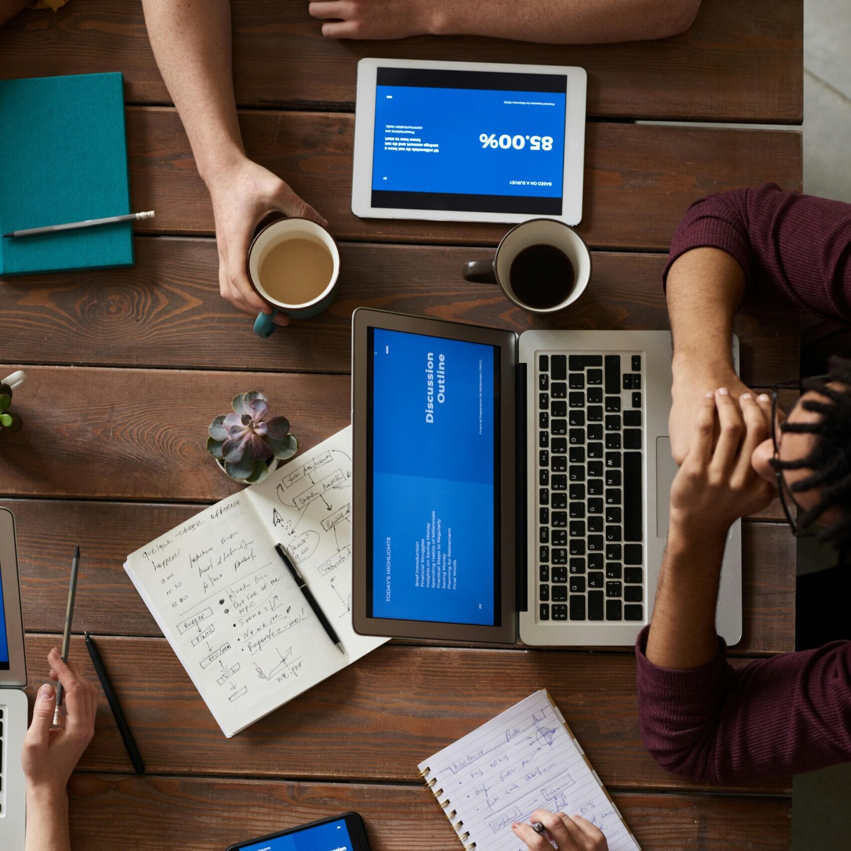 Group of coworkers discussing business strategies with laptops and tablets in a modern office setting.